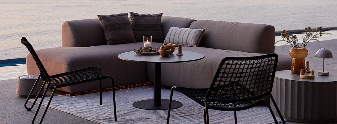 Allwetter-Loungesofa und Lounge-Stühle auf einer Terrasse bei Sonnenuntergang
