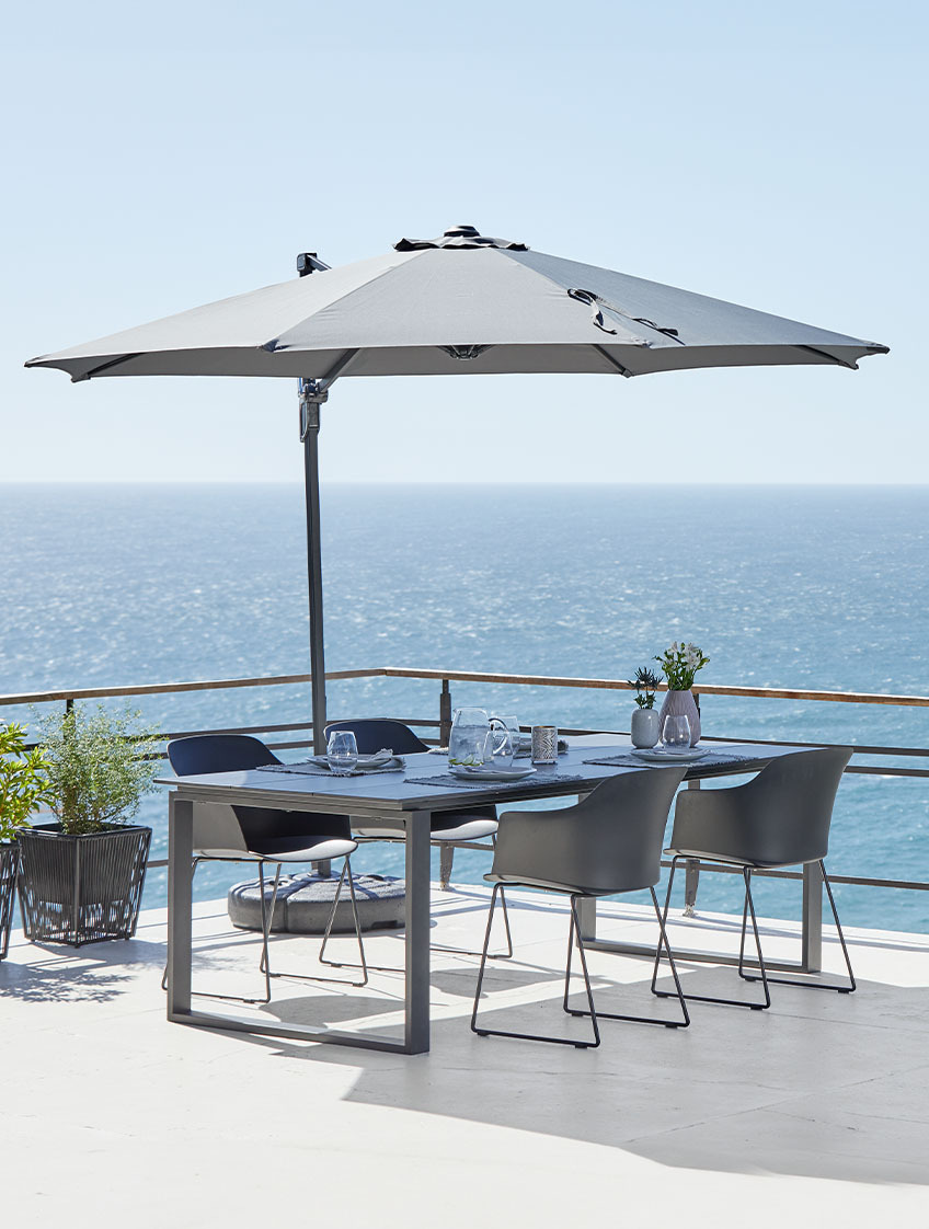 Großer hängender Sonnenschirm, Gartentisch und Stühle auf Terrasse am Meer