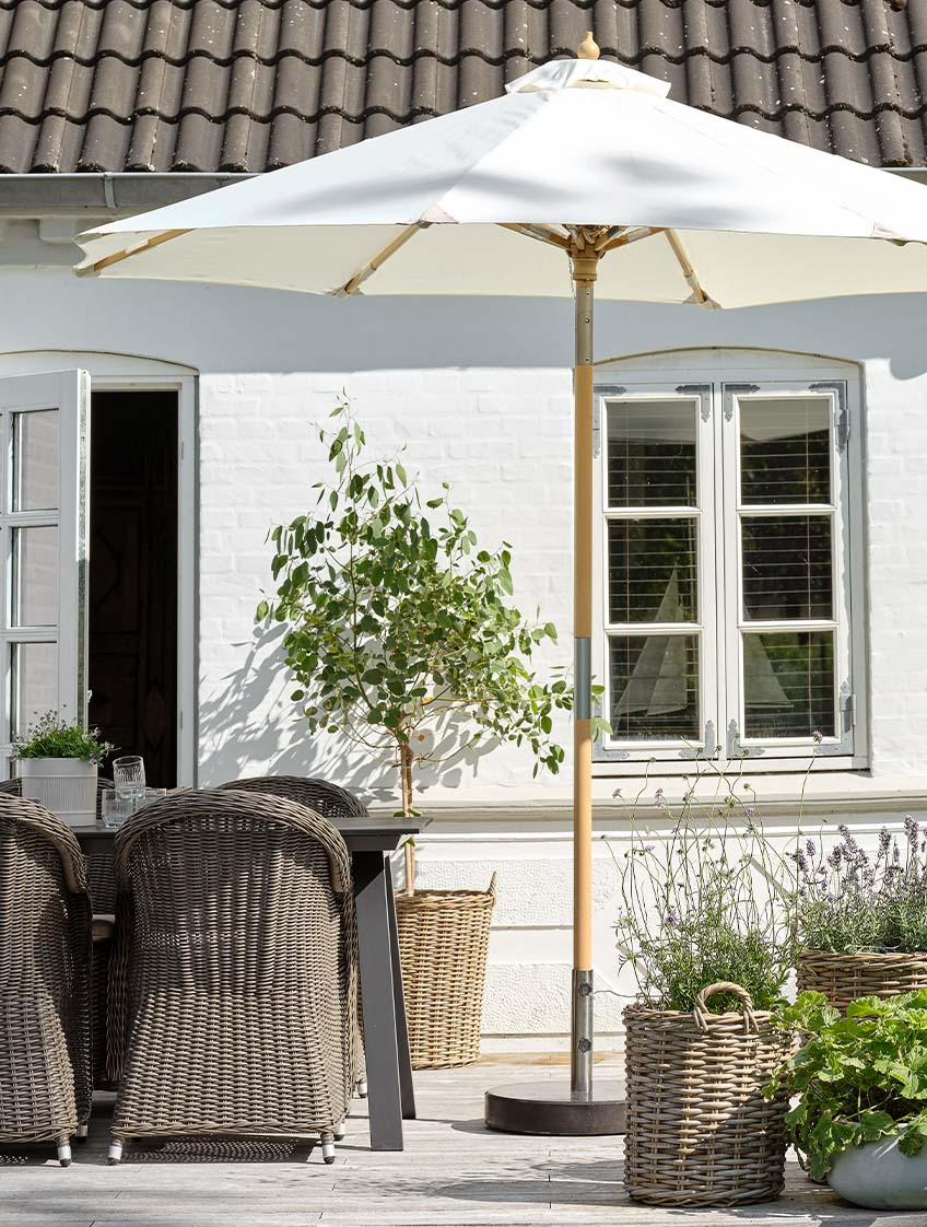 Klassisch cremefarbener Sonnenschirm auf Terrasse mit Gartentisch und -stühlen