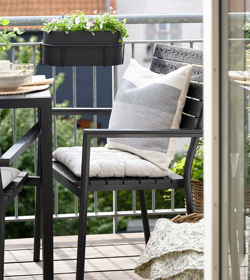 Ein stapelbarer Gartenstuhl in Schwarz mit Sitzkissen auf dem Balkon